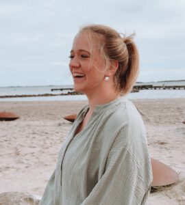 Sophia sitzt lachend am Strand und ist dankbar, dass sie die schwere Depression überwunden hat und endlich ein Leben lebt, dass ihrer wahren Essenz entspricht.