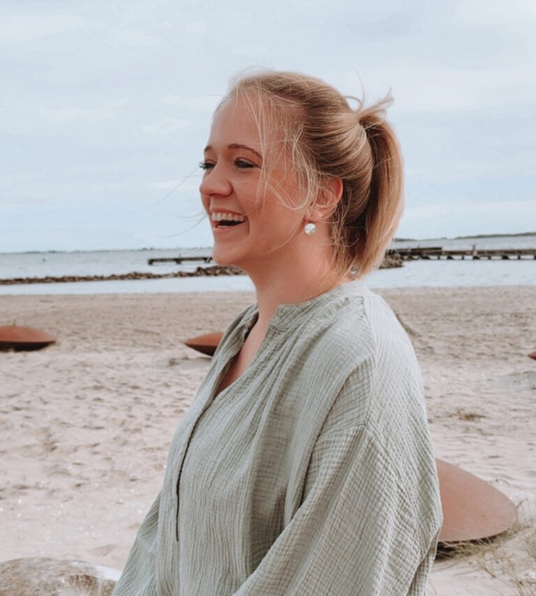 Sophia sitzt lachend am Strand und ist dankbar, dass sie die schwere Depression überwunden hat und endlich ein Leben lebt, dass ihrer wahren Essenz entspricht.