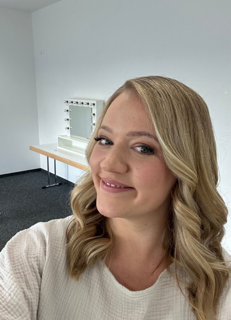 Sophia lächelt in die Kamera, hat lockiges Haar und befindet sich im Stylingraum der Filmstudios in Köln. Sie hat gerade ihre Komfortzone verlassen und ist total stolz und glücklich.