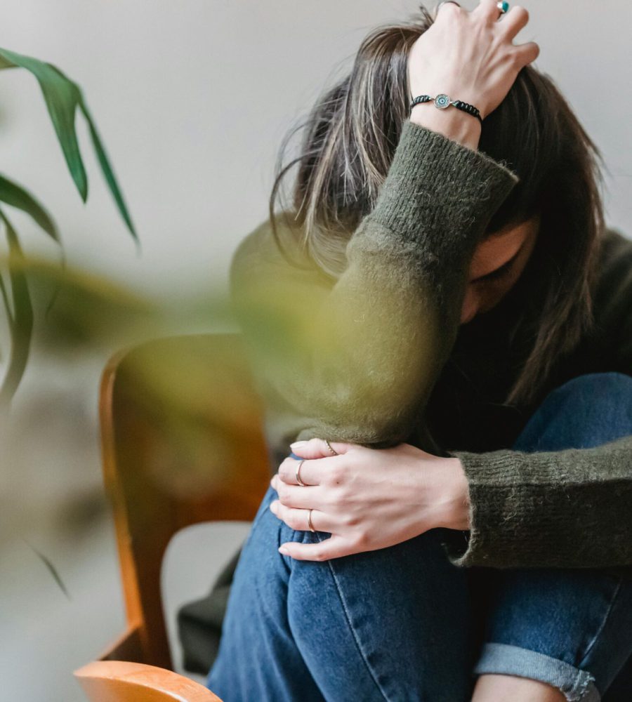 Eine junge Frau sitzt zusammengerollt auf einem Stuhl, hält den Kopf in der Hand und wirkt erschöpft – ein Zeichen für Stress und emotionale Belastung. Mit einem ganzheitlichen Coaching kann sie neue Wege finden, um innere Balance und mehr Lebensfreude zu gewinnen.