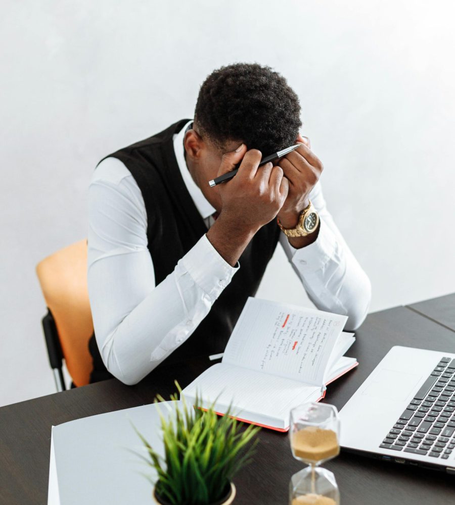 Ein gestresster Mann sitzt an einem Schreibtisch mit Laptop, hält sich den Kopf und wirkt überfordert – ein Zeichen für hohen Druck im Arbeitsalltag. Ein individuelles & ganzheitliches Coaching kann helfen, Stress besser zu bewältigen und wieder mehr Leichtigkeit in den Alltag zu bringen.