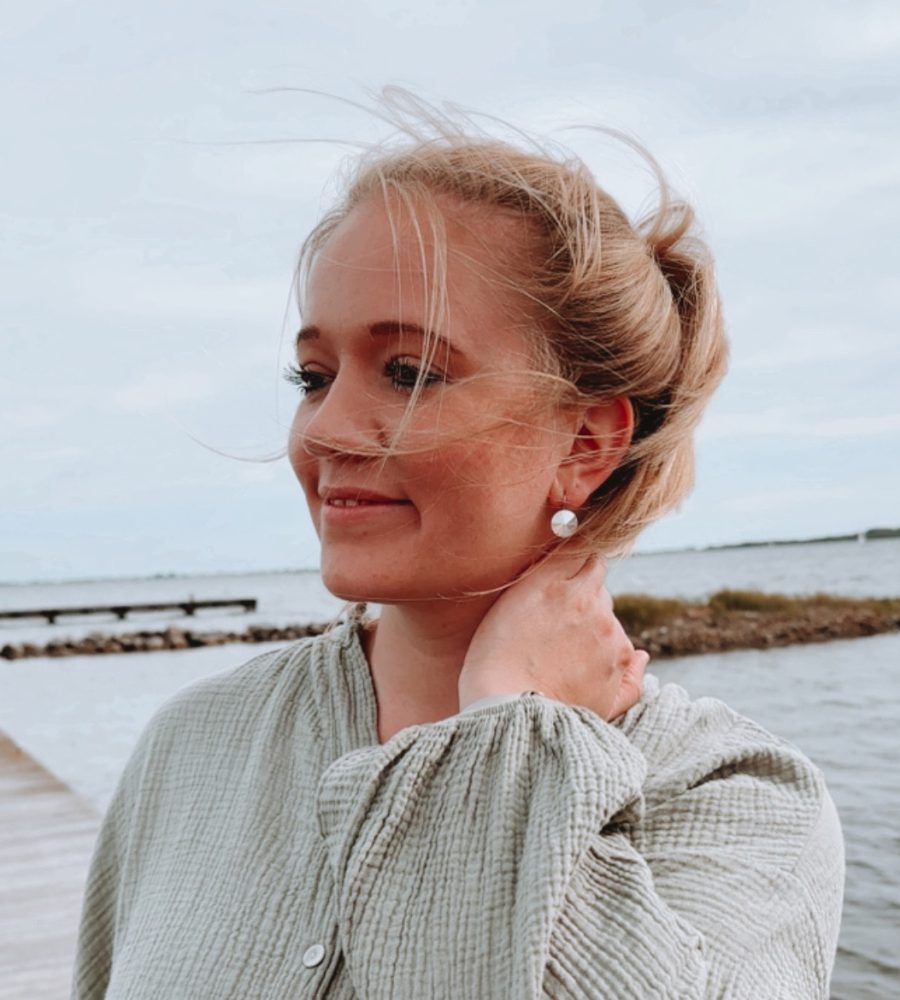 Life Coach Sophia steht entspannt am Meer, lächelt sanft und strahlt Ruhe aus – ganzheitliches Coaching für mehr Selbstbestimmung, Resilienz & Lebensfreude