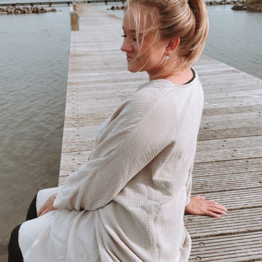 Sophia sitzt ruhig & reflektiert auf einem Steg am Wasser und genießt die Natur mit geschlossenen Augen.