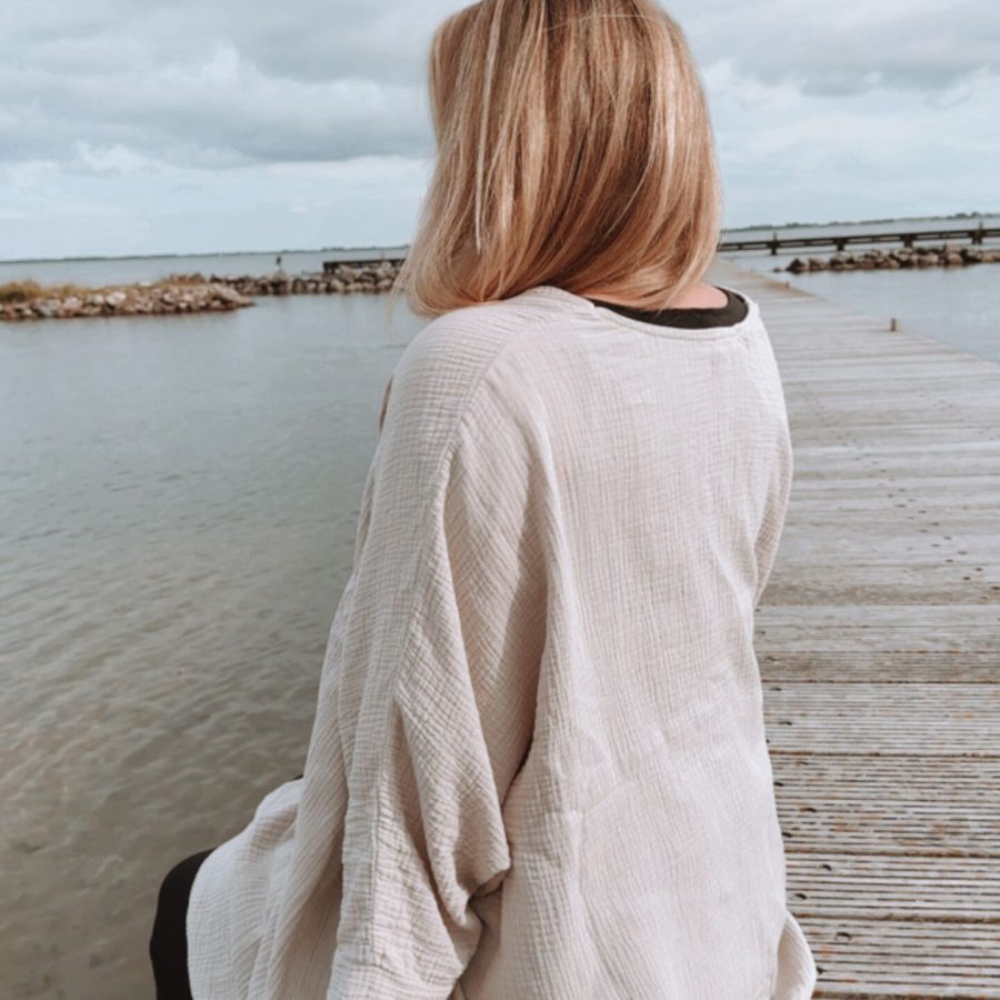 Life Coach Sophia sitzt auf einem Steg am Wasser und schaut aufs weite Meer in vollkommener Ruhe & Gelassenheit