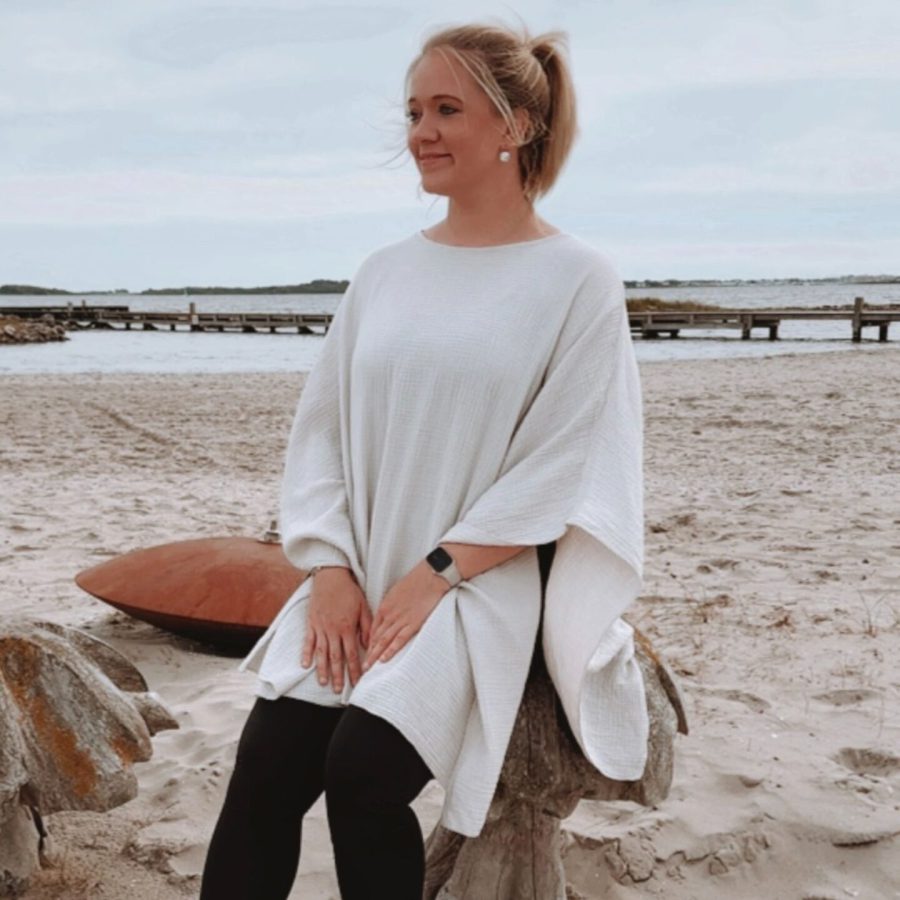 Sophia sitzt barfuß im Sand am Meer und schaut in die Ferne. Sie genießt die Ruhe, die Natur und ist vollkommen entspannt.