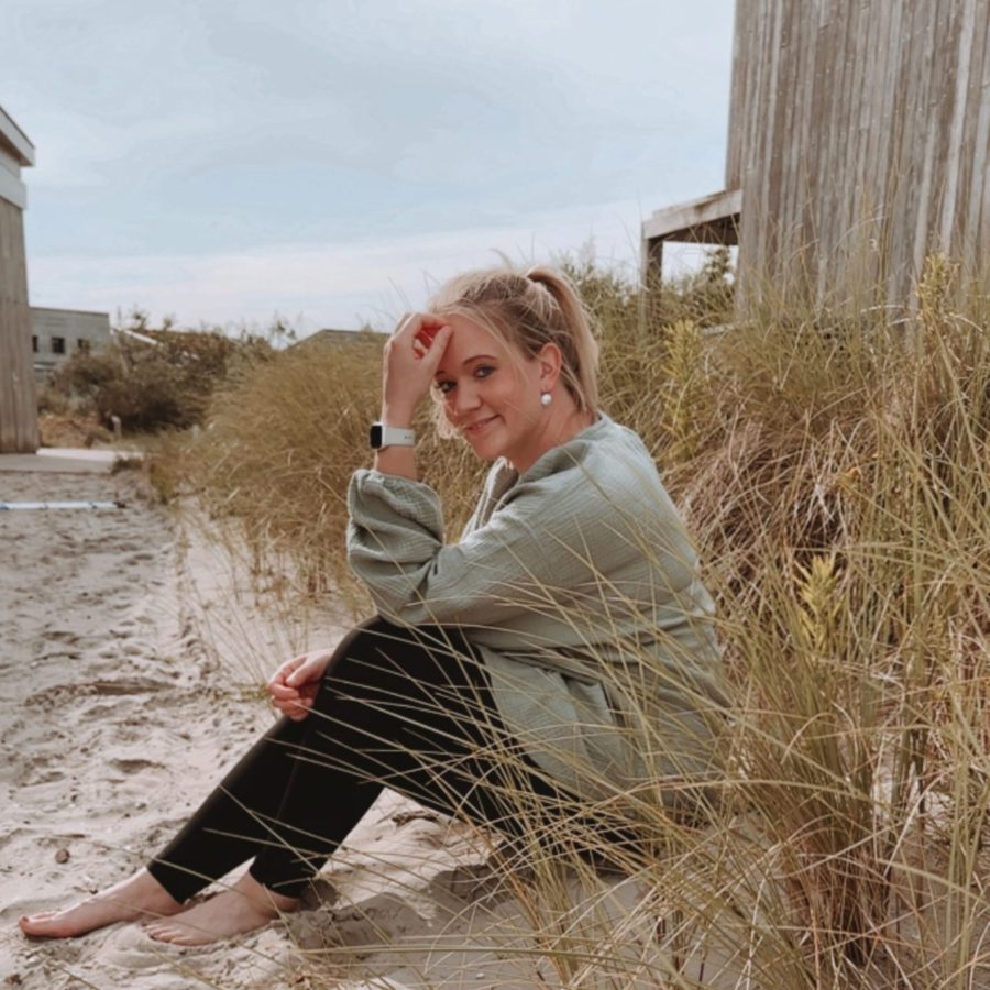 Sophia sitzt barfuß im Sand zwischen Dünengras, lächelt und ist innerlich zufrieden – diese Entspannung , Ruhe & Zufriedenheit vermittelt sie in ihrem ganzheitlichen Life Coaching