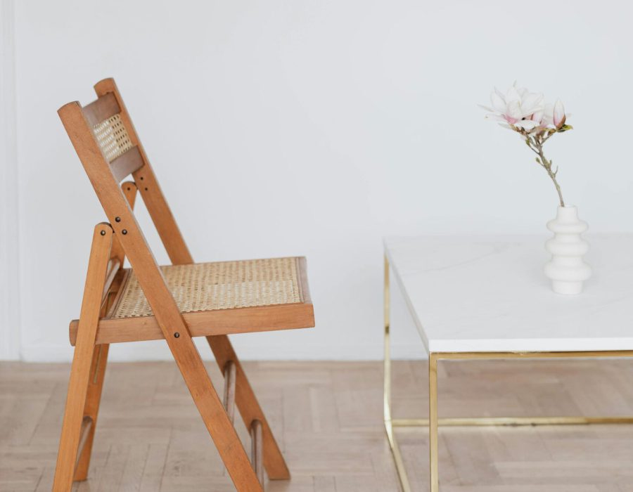Ein schlichter Holzstuhl steht vor einem eleganten Tisch mit einer zarten Blume in der Vase – Symbol für einen ruhigen, klaren Raum zum Innehalten und neue Impulse sammeln, genau wie in einer 1:1 Einzelsession bei Sophia