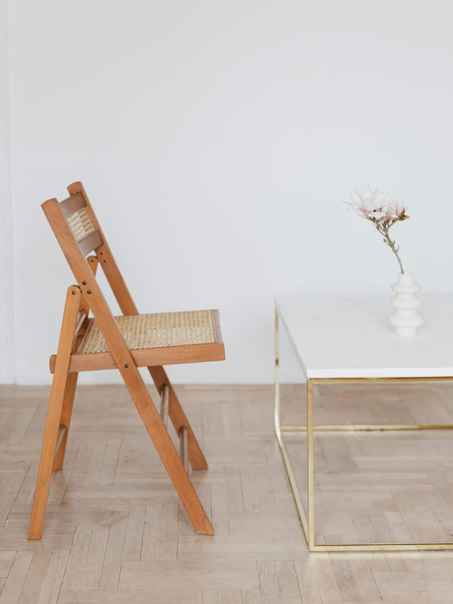 Ein schlichter Holzstuhl steht vor einem eleganten Tisch mit einer zarten Blume in der Vase – Symbol für einen ruhigen, klaren Raum zum Innehalten und neue Impulse sammeln, genau wie in einer 1:1 Einzelsession bei Sophia