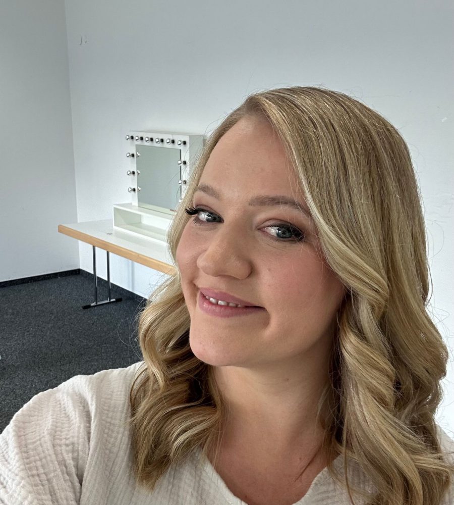 Sophia lächelt in die Kamera, hat lockiges Haar und befindet sich im Stylingraum der Filmstudios in Köln. Sie hat gerade ihre Komfortzone verlassen und ist total stolz und glücklich.